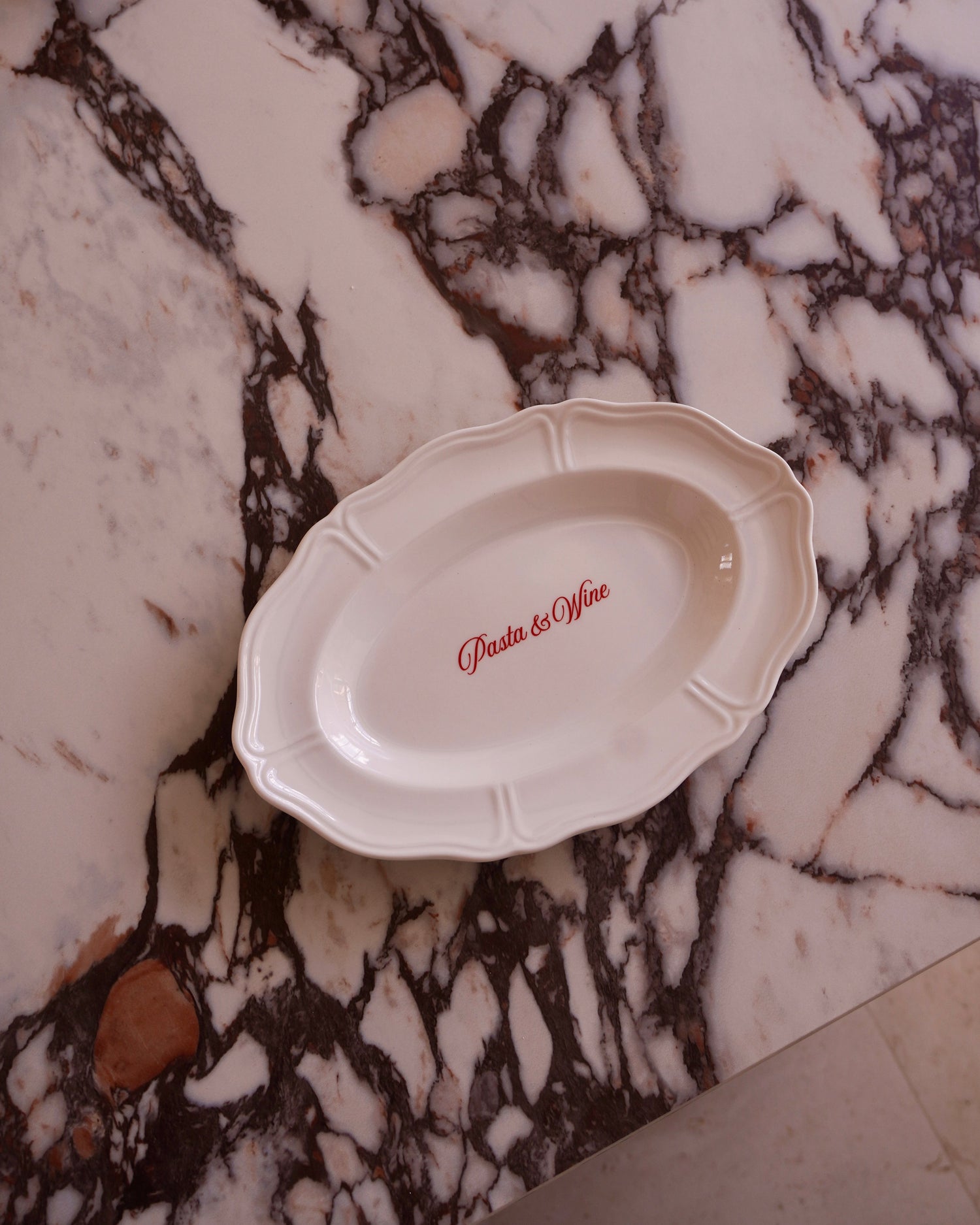 White oval dish with 'Pasta & Wine' text on a marble surface